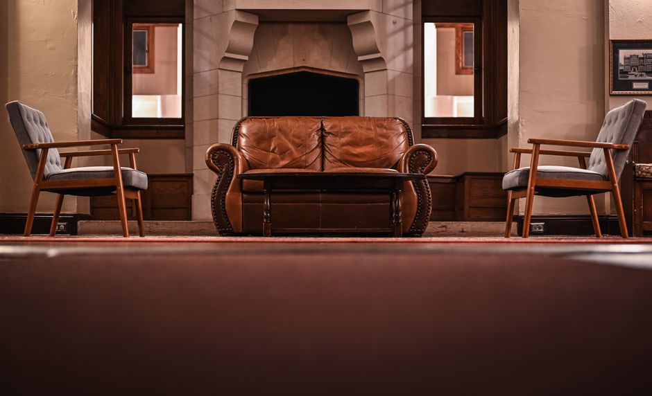 A vintage style living room featuring a leather couch, armchairs, and a classic fireplace.